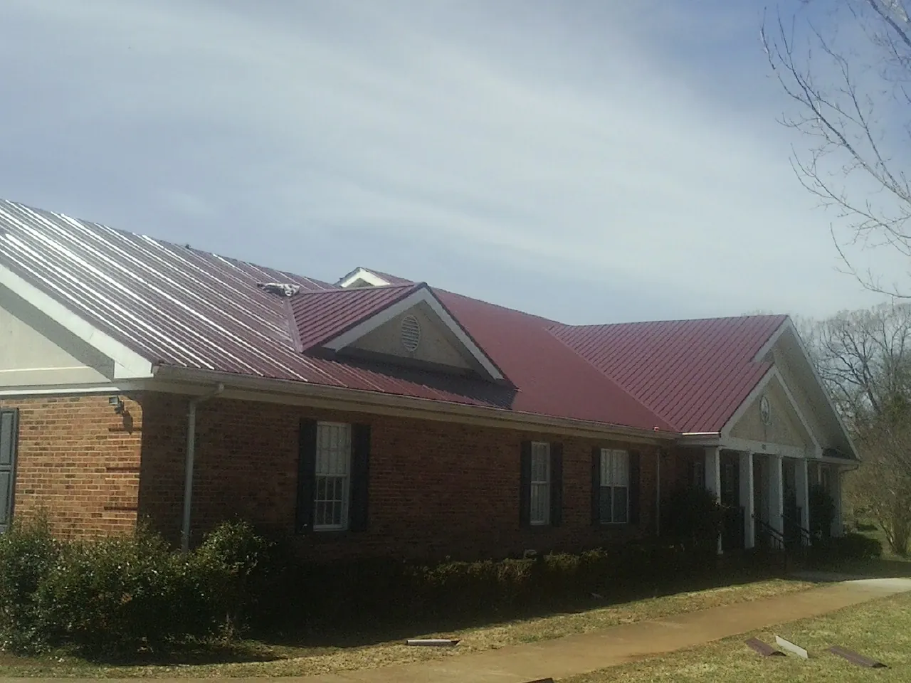 Red metal roof with gabled entries on a long brick building, from a Hail Damage Roof Repair job in Cathlamet