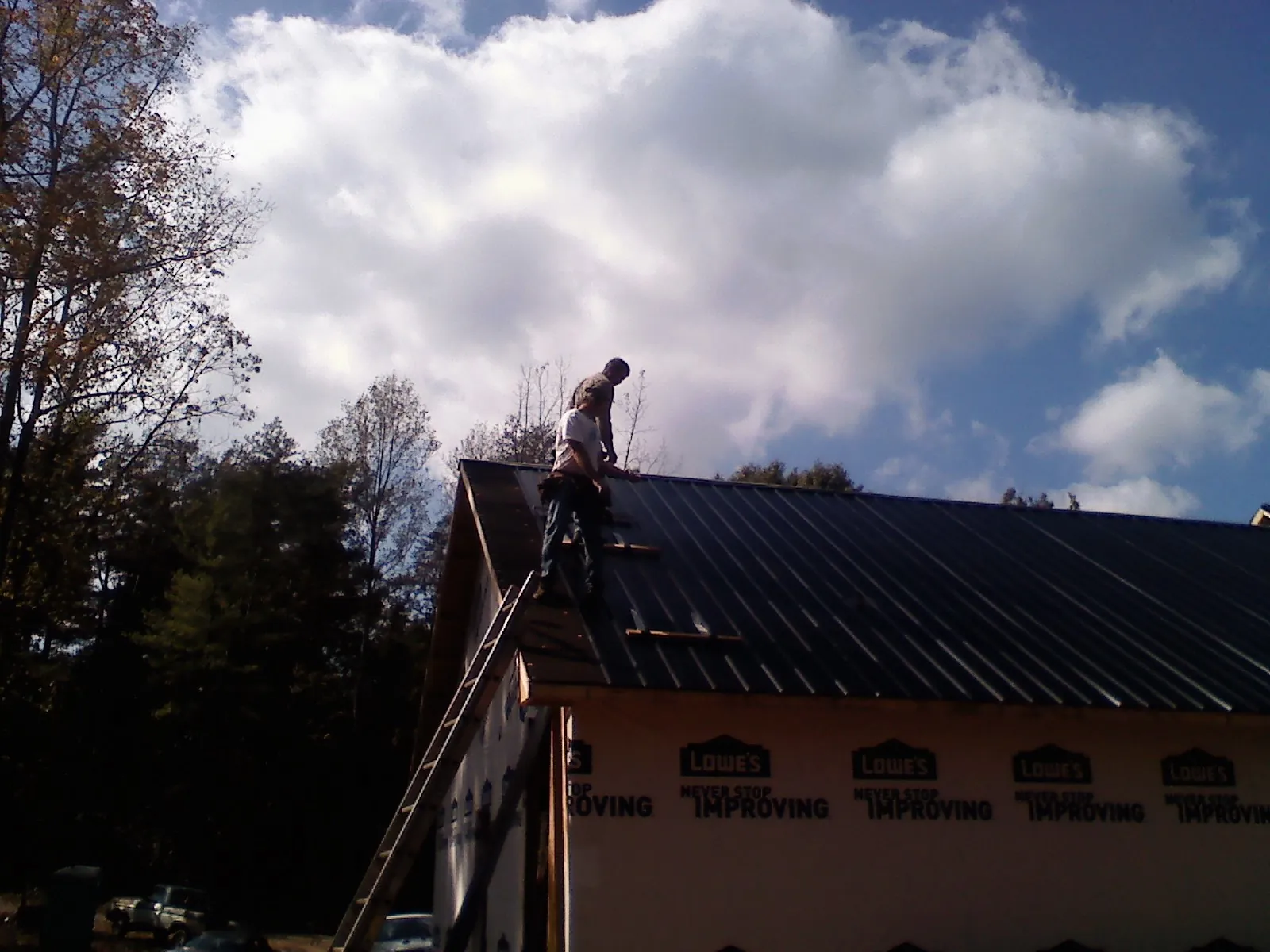 Roofer fastening dark metal panels high against a cloudy sky, from a Roof Inspection job in Cathlamet