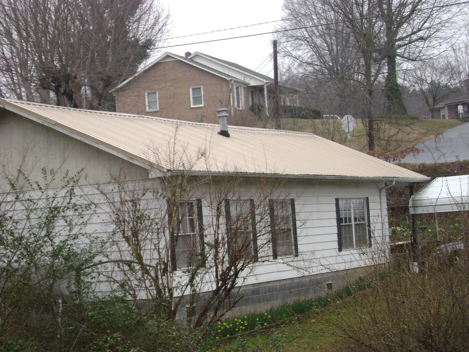Tan metal roof on a white sided house set into a hillside — Commercial Roofing by Roofing Brothers in Cathlamet